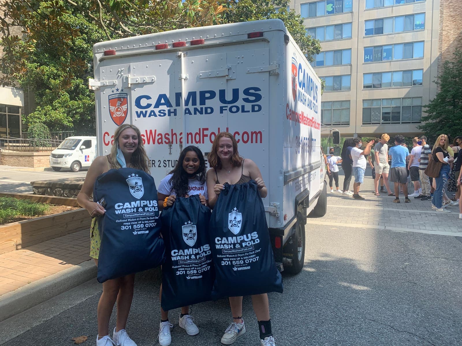 American University students holding Campus Wash and Fold branded laundry bags next to the Campus Wash and Fold truck outside Letts Hall in Tenleytown, Washington DC